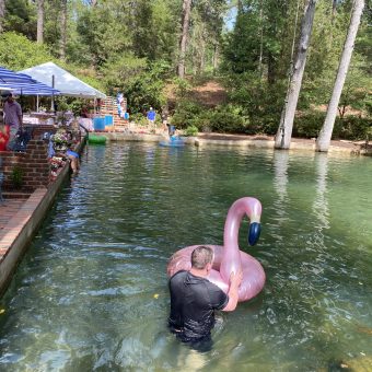 A man in black jacket riding on the back of pink flamingo.
