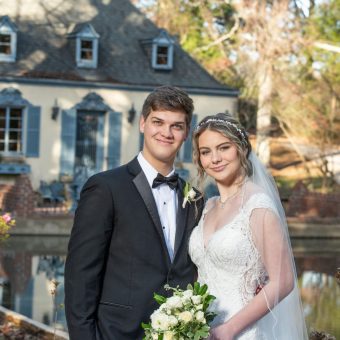 A young couple poses for a picture in front of a house.