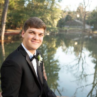 A young man in a tuxedo standing next to a lake.