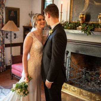 A bride and groom pose for a picture in front of the fireplace.