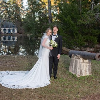 A bride and groom pose for a picture in front of an old cannon.