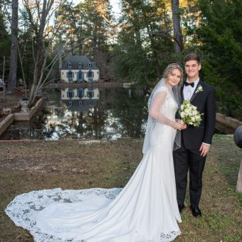 A bride and groom pose for a picture in front of the pond.