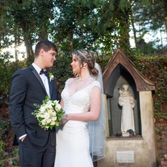 A bride and groom standing in front of a statue.